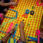 People around a table weaving colored tape into a plastic net