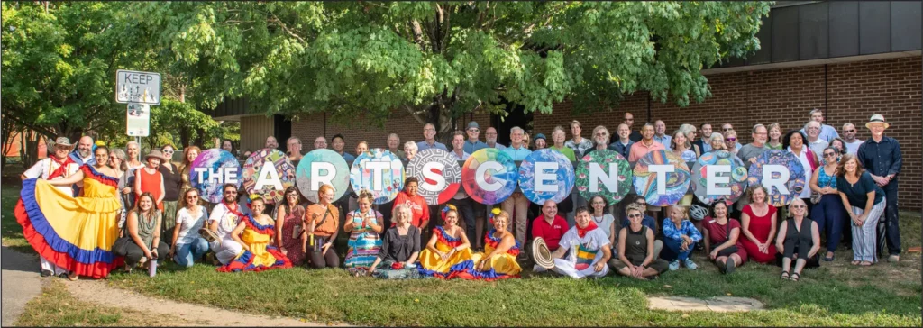 Large photo with at least two dozen people standing in front of the new ArtsCenter location, holding letters that spell "The ArtsCenter"