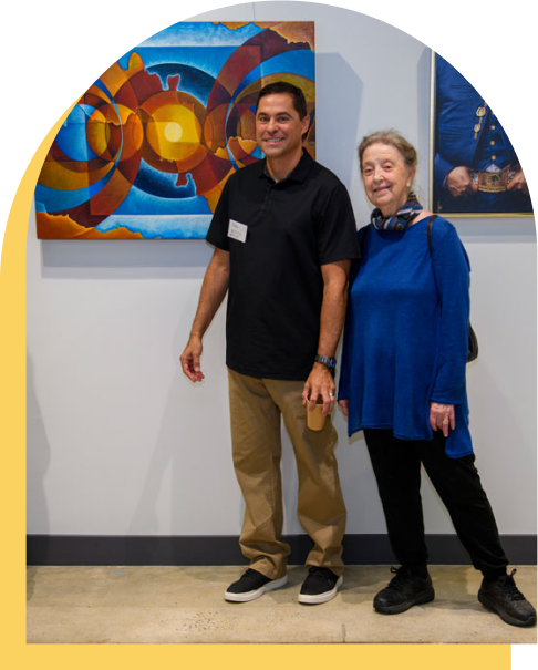 Two adults smiling in front of colorful painting at an art gallery