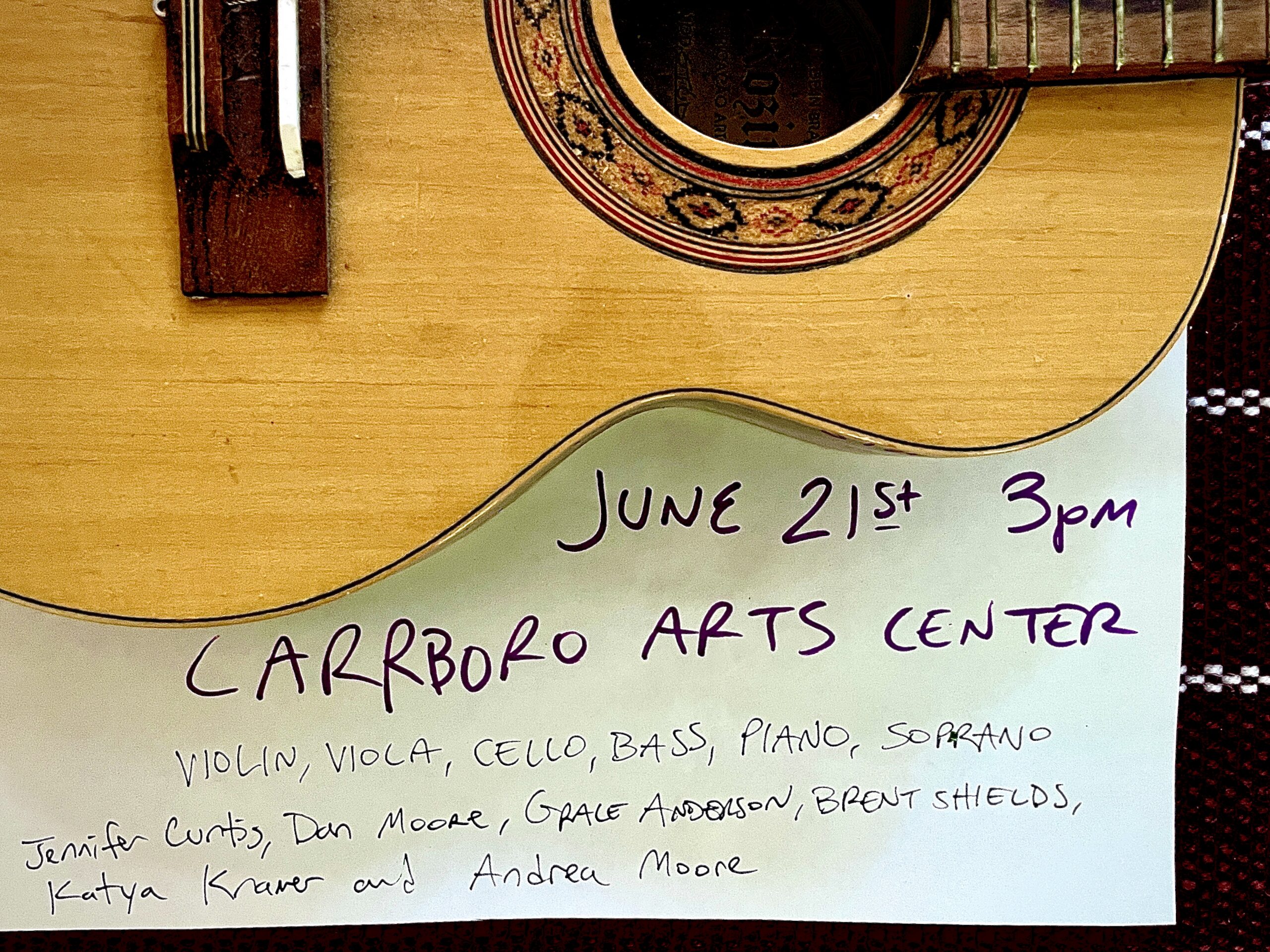 A handwritten sign on a guitar reads: June 21st 3pm, Carrboro Arts Center. Violin, viola, cello, bass, piano, soprano: Jennifer Curtis, Dan Moore, Grace Anderson, Brent Shields, Katya Kramer and Andrea Moore.