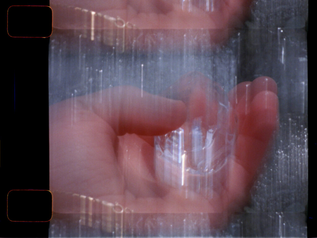 A hand holds a clear object; the image is blurry with overlapping frames, giving a double-exposure effect.