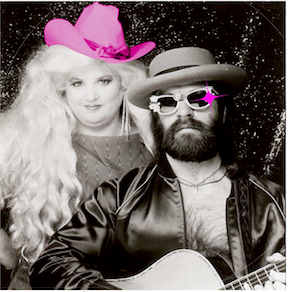 A woman in a pink hat stands next to a bearded man in sunglasses and a hat, holding a guitar.